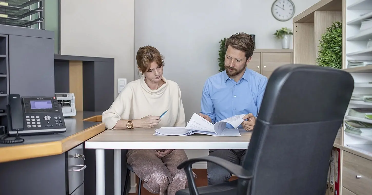 Koppel bespreekt hospitalisatieverzekering met een adviseur van Alitos Vlaanderen aan een tafel.