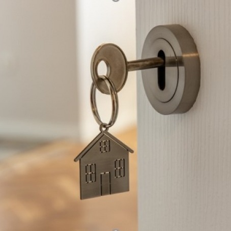 Sleutel met huisvormige sleutelhanger in een slot, symbool voor woningfinanciering.